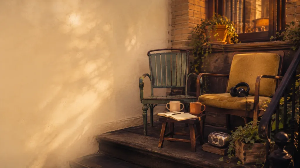 Two porch chairs with coffee mugs, an open notebook, headphones, and a small radio on a stoop